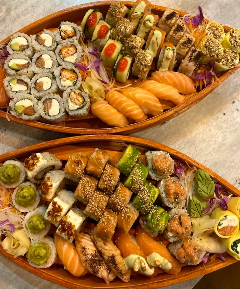 Dos canoas de madera con rolls de salmón y palta, niguiris de salmón y piezas coronadas con guacamole