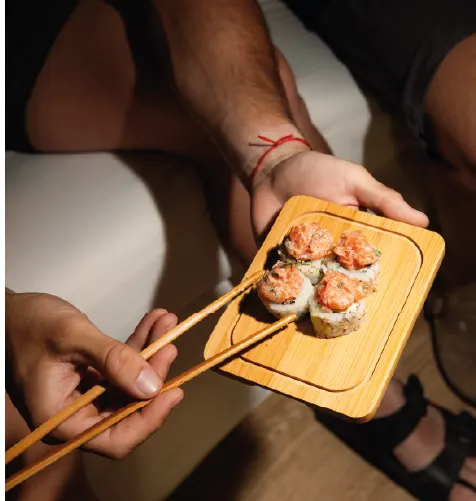Cuatro piezas de roll coronadas con salmón, servidas en una tablita de madera