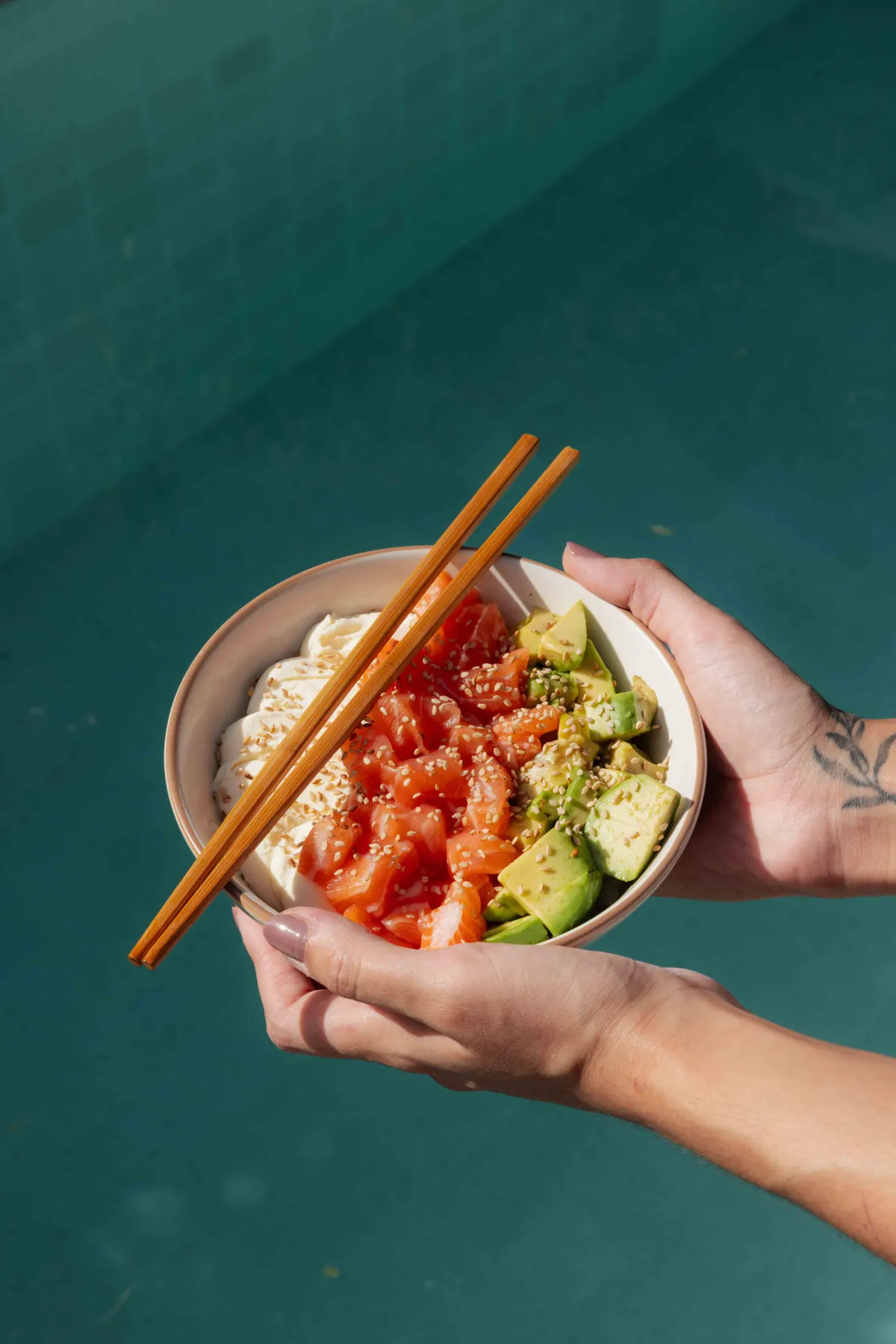 Salad de Suteki con cubos de salmón, palta, queso philadelphia y sésamo, en un bowl sostenido con las dos manos y palitos de madera encima